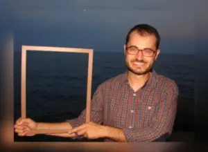 Especialista en salud mental en Barcelona, David Gonzalez sosteniendo un marco con el mar al anochecer a sus espaldas, simbolizando la ruptura de esquemas.
